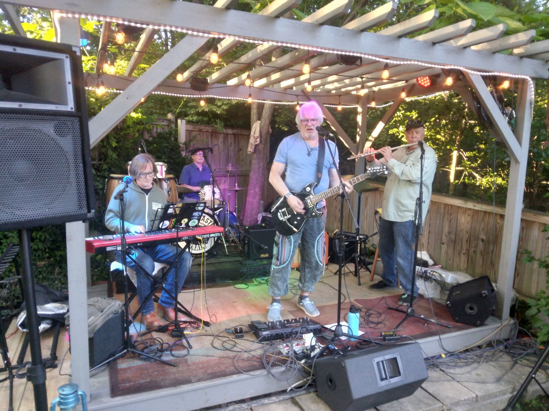 Frank Oelschlager on electric guitar leading a full band jam under a lit backyard pergola