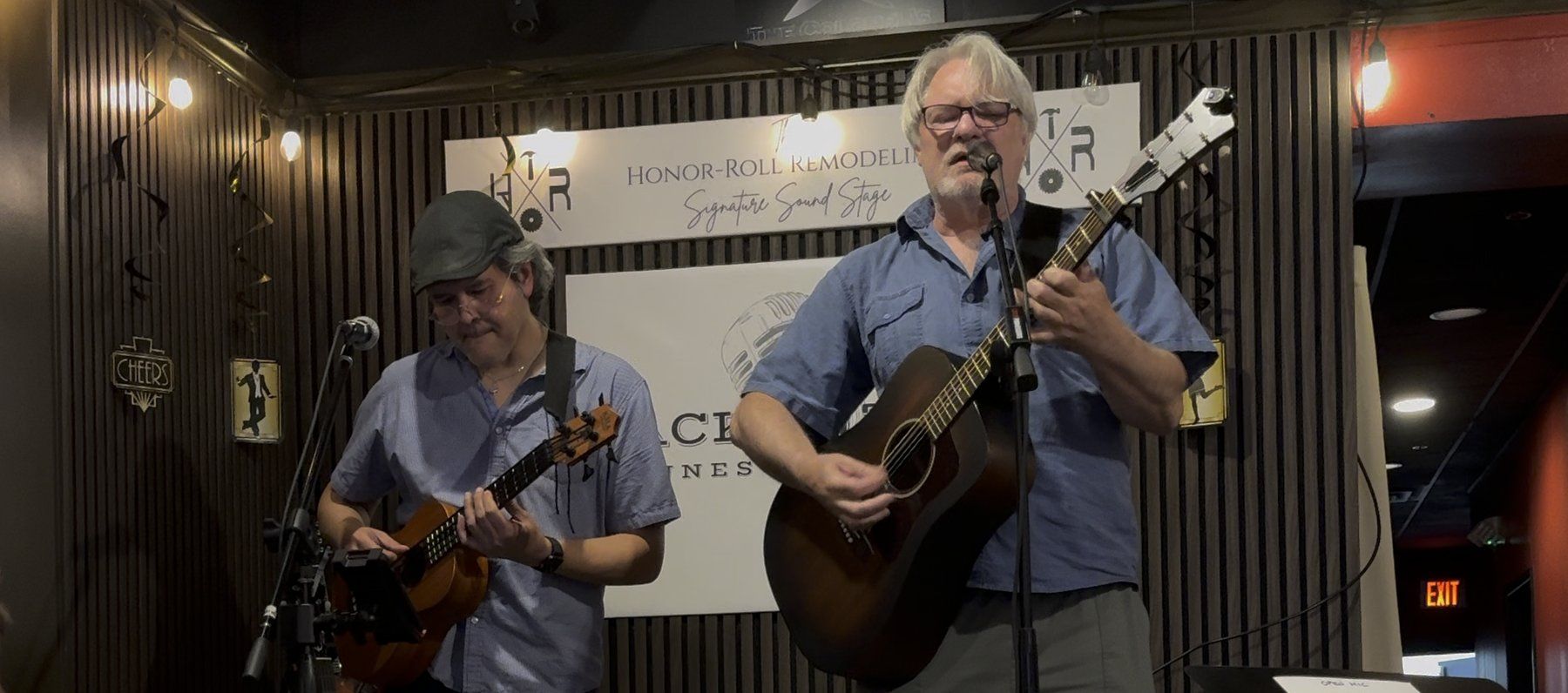 Frank Oelschlager singing with acoustic guitar, accompanied on bass, at an intimate club stage