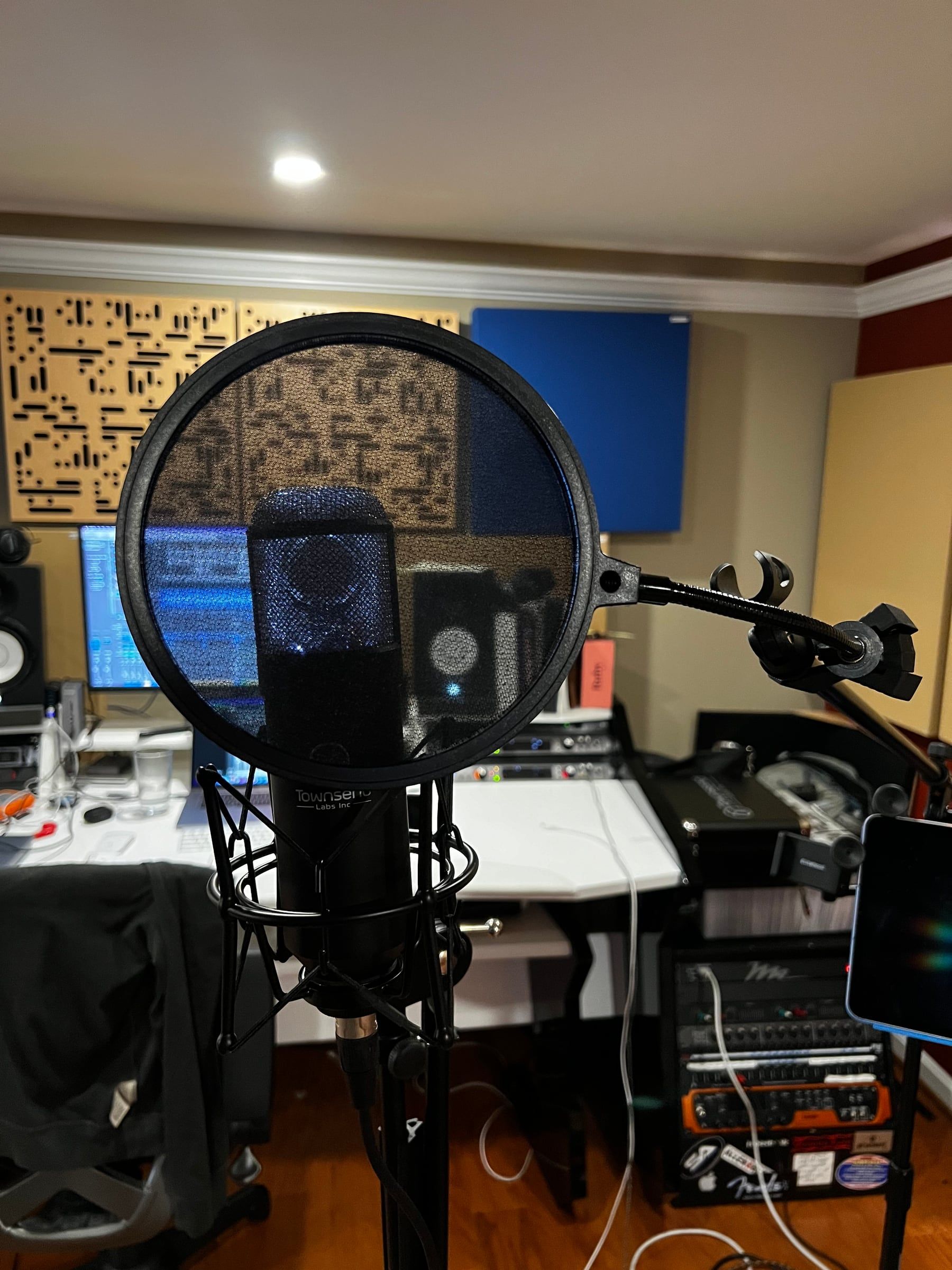 A condenser microphone with a pop filter, with the mixing desk, monitors, and a rack of outboard gear behind it